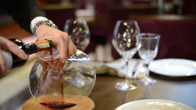 The man hand pouring the red wine from bottle  into the decanter in restaurant