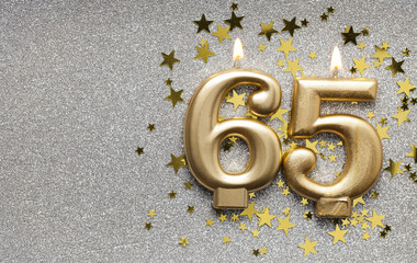 Number 65 gold celebration candle on star and glitter background