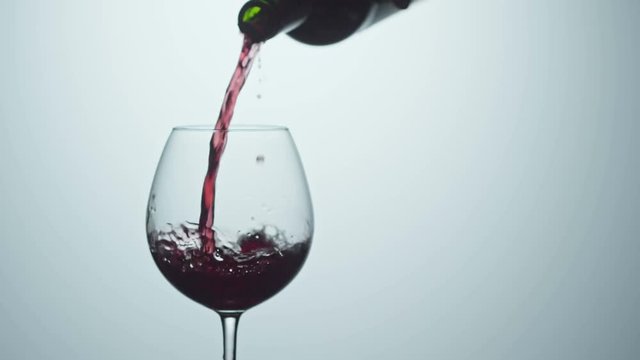 Cinemagraph of pouring red wine into wineglass from bottle. Studio shot