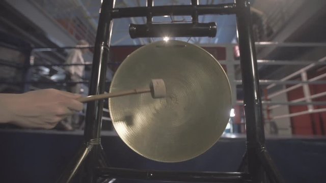 Male hand with hammer banging a native golden gong in slowmotion. Beginning, start concept.