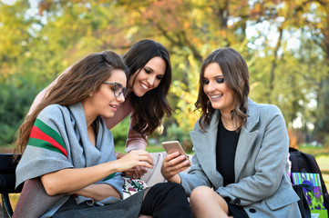Obraz premium three girlfriends surfing with mobile phone in a park on a bench