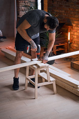 Carpenter drilling a hole in a board in a room with loft interio