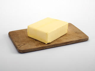 Block of butter on wooden chopping board, white background