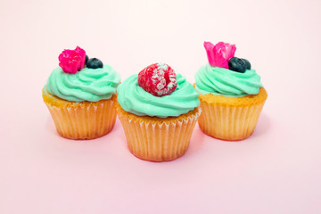 Cupcakes with butter cream and vanilla with blueberry and raspberry with pink flowers on pink background