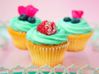 Cupcakes with butter cream and vanilla with blueberry and raspberry with pink flowers on pink background