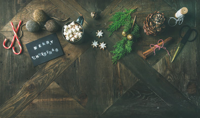 Christmas or New Year holiday celebrating background. Flat-lay of greeting card, glittering toys, hot chocolate, cinnamon, candy cane, scissors over vintage wooden table, top view, copy space