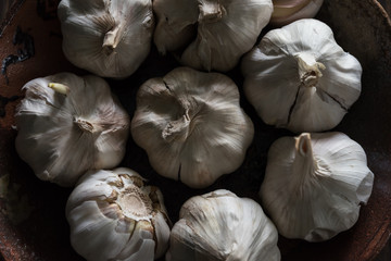 Garlic in a cup is in a low light on a wooden floor.