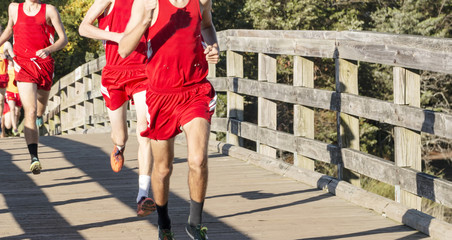 Boys high school cross country runners going over a wooden bridge