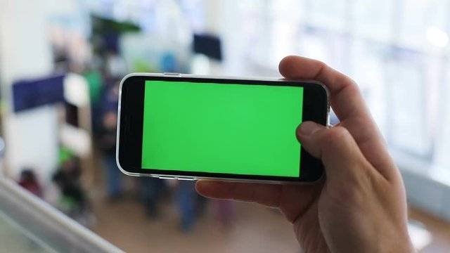 man hand horizontal holding smart phone closeup green screen chromakey blurred background airport male review technology appstore apps video call ebook network ebusiness digital device online mockup