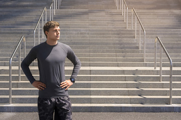 Young man in sportswear in urban place standing resting after exercises, city in sunnyday.