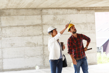 Female inspector and architect walk with head engineer trough construction site.