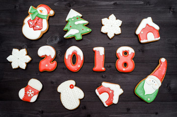 Happy new year 2018 sign symbol and red and white gingerbread cookies on dark wooden background. Top view, flat lay. Christmas cookies, santa, snowman, snowflake, house, christmas sock, free space