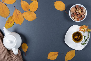 Sheet of brown craft paper, white envelope with note and flower, yellow and orange leaves, color pencils, cup of herbal tea and candies on gray background. Colorful autumn mock up. Top view.