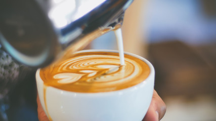 barista pouring streamed milk to make heart shape latte art in cup of hot coffee, retro tone