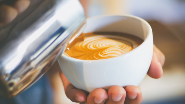 barista pouring streamed milk to make heart shape latte art in cup of hot coffee, retro tone