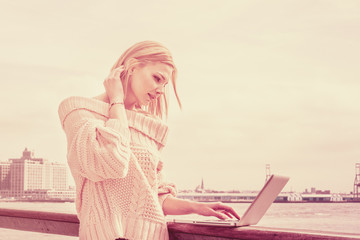 Eastern European Business Woman traveling, working in New York. Wearing loose sweater, an American college student reading, working on laptop computer by river. Copy Space. Vintage filtered effect..