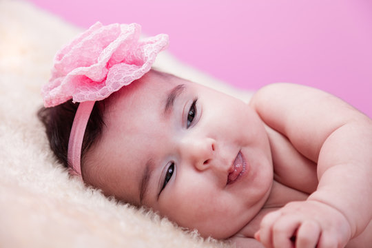 Cute, pretty, happy, chubby baby girl portrait smiling and playful sticking tongue. Naked or nude on fluffy blanket. Pink flower headband. Four months