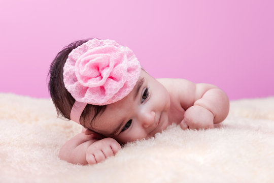 Cute, pretty, happy and chubby baby girl without clothes, naked or nude, lying down a fluffy blanket with pink flower headband. Four months old