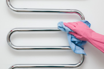 Employee's hand in protective glove with rag wiping chrome heated towel rail in bathroom. Maid or housewife cares about house. Spring general or regular clean up. Commercial cleaning company concept.