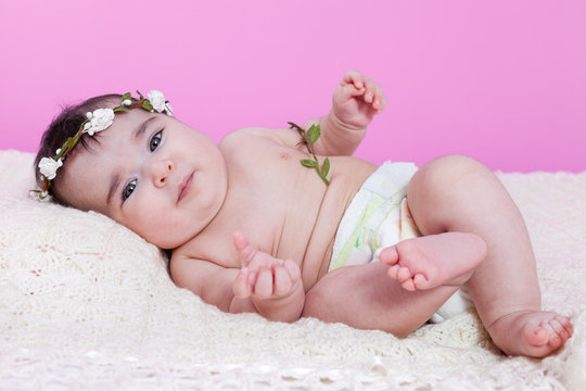 Cute, pretty, happy, chubby baby girl, naked or nude with diaper or nappy, on a fluffy blanket wearing a floral wreath headband or headdress. Four months old
