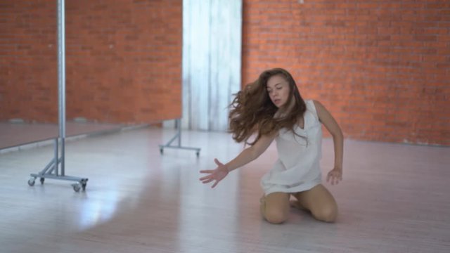A professional dancer dances in the ballroom in front of a mirror. a woman is tumbling on the floor. young attractive girl is exercising indoors on the background of a kerf wall. the woman is wearing