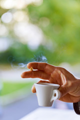 close up man's hand with cup of black coffee and a cigarette
