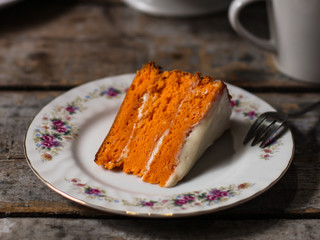 piece of orange cake with white cream on a wooden table