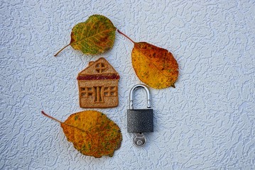 ключ с замком и домик из печенья с сухими опавшими листьями на сером фоне