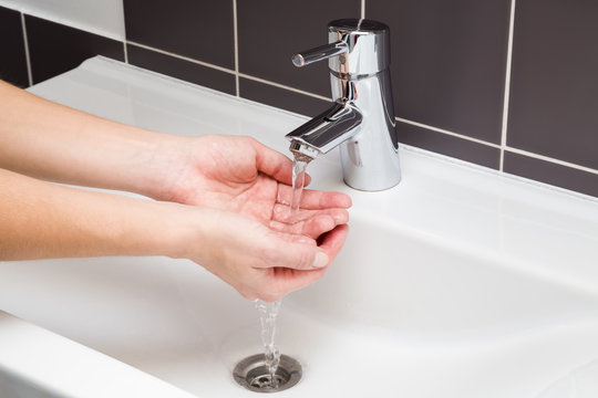 Hygiene. Woman washing her hands in the ceramic sink under the water tap. Water running. Healthy lifestyle concept.