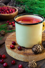 Drink juice from cranberries in an iron cup on a dark background with spruce branches and cones with copy space concept of cold and warming medicinal drinks