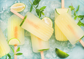 Summer refreshing lemonade popsicles with lime and mint with chipped ice over blue background, top view