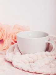 Big white mug with coffee or tea tucked with a soft blanket next to roses on pink marble desk. Copy space