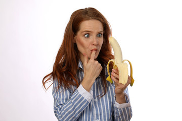 Hübsche rothaarige Frau mit Banane leckt sich einen Finger