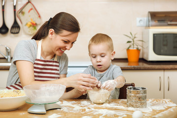 Little kid boy helps mother to cook Christmas ginger biscuit in light kitchen with tablet on the table. Happy family mom 30-35 years and child 2-3 in weekend morning at home. Relationship concept