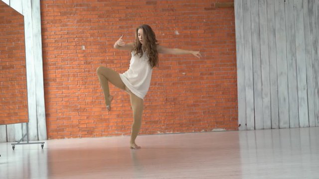 A professional dancer dances in the ballroom in front of a mirror. a woman is tumbling on the floor. young attractive girl is exercising indoors on the background of a kerf wall. the woman is wearing