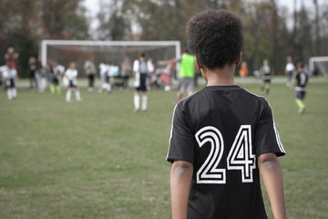 Young african american boy watching friends play football soccer game - Powered by Adobe