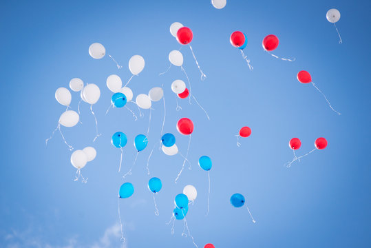 Balloons of red blue and white colors flying in the blue sky with clouds