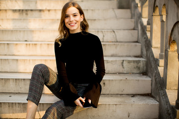 Young woman with mobile phone sitting at stairs outdoor