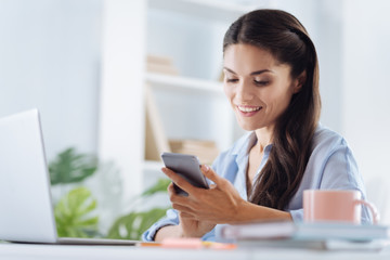Positive self employed woman using her smartphone
