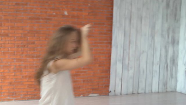 A professional dancer dances in the ballroom in front of a mirror. a woman is tumbling on the floor. young attractive girl is exercising indoors on the background of a kerf wall. the woman is wearing