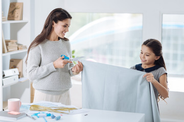 Pleasant young woman cutting a piece of cloth