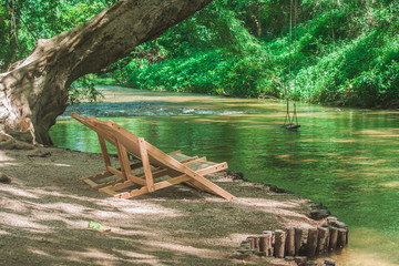 Relaxation Concept : Close up brown wooden bench or armchair on small rocks beside the river with green natural background.