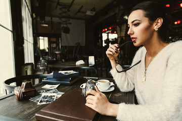 Woman looks thoughtful sitting at the table with old photos in the cafe