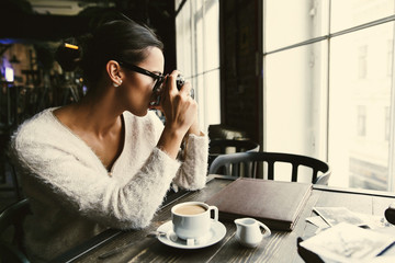 Woman takes a picture on retro photocamera sitting in the cafe