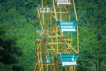 Vintage retro image close up part of colorful ferris wheel with green trees background at green park.