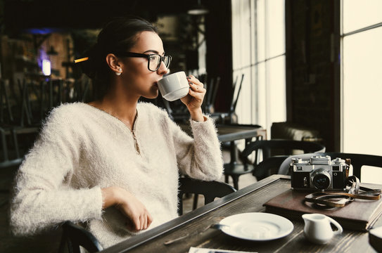 Pretty young woman sits with cup of coffee at the table with camera in the cafe