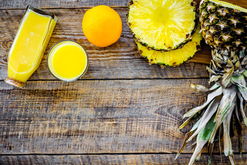 Tropical fruits juice. Bottle with beverage near pineapples slices and oranges on wooden background top view copyspace