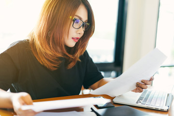 Asian stylish glasses woman designer wear black dress and red lips working with her laptop and checking the document in selective focus..