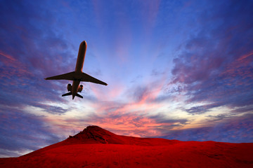 Samolot pasażerski, odrzutowy leci o zachodzie słońca nad pustynią.