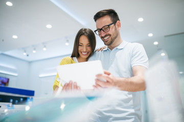 Buying new tablet at tech store. Looking for a new peace of tech gadget. Couple in shopping.